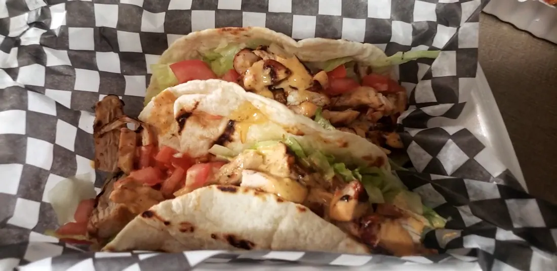 Two jerk chicken tacos in a checkered paper basket