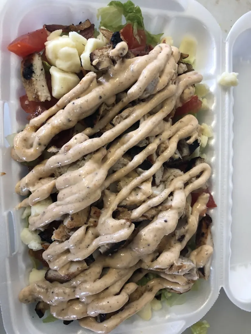 Jerk chicken over greens in a takeout container, drizzled with jerk mayo