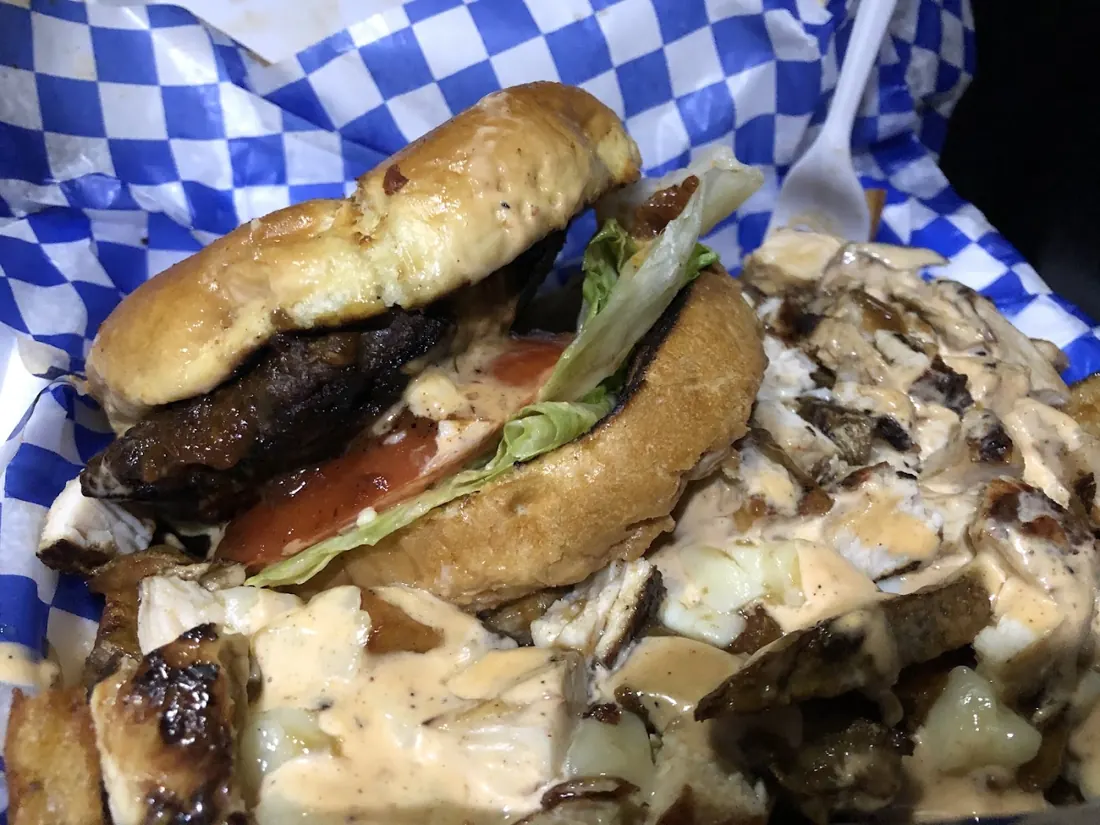 Burger-style sandwich topped with jerk chicken on a blue checkered cloth